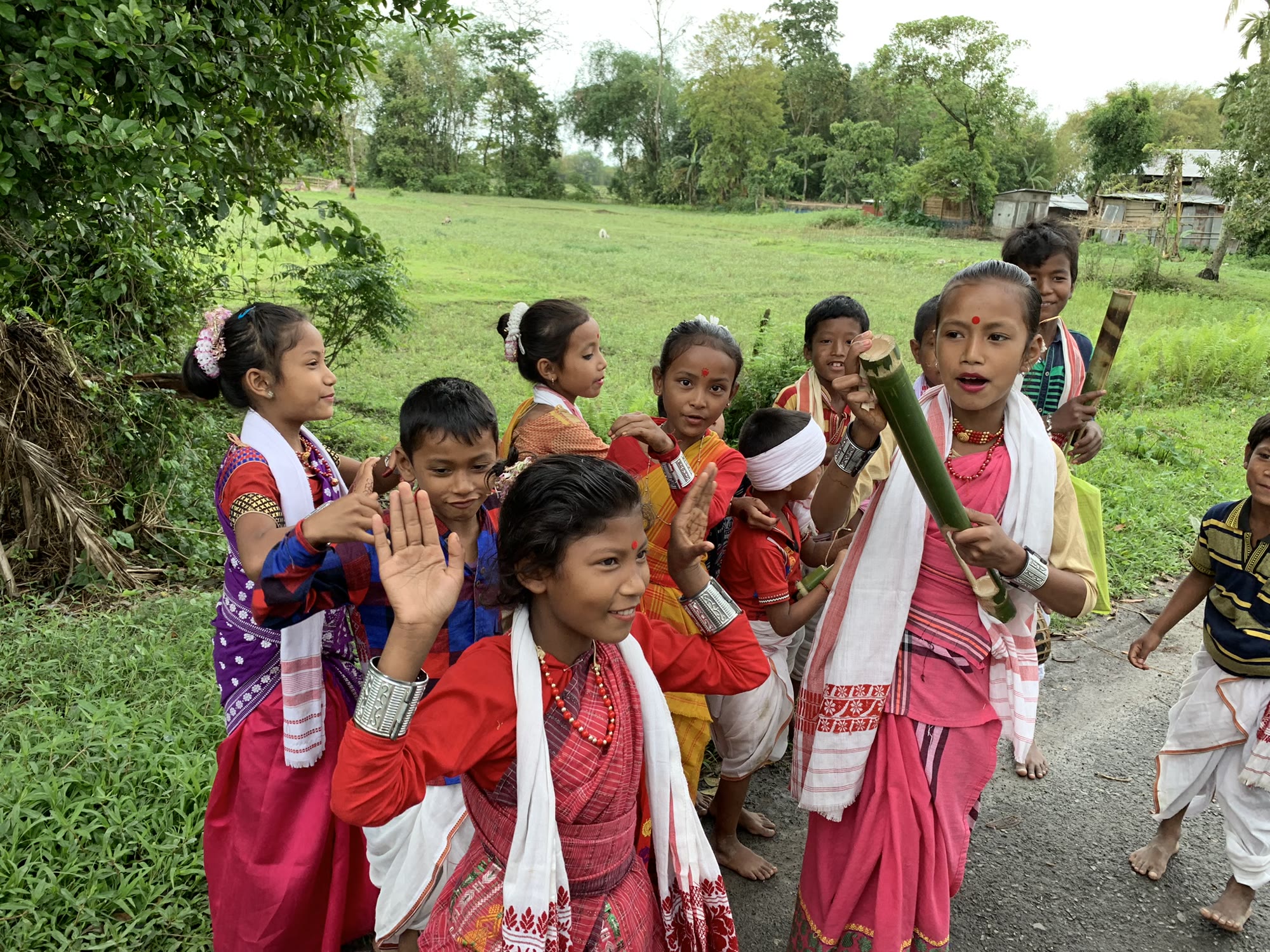 Children in traditional Assamese dress greeting visitors on a village road near Kaziranga National Park