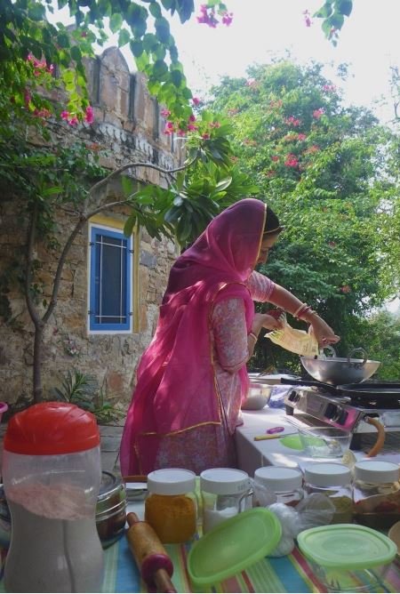 A host in a pink sari preparing bread at an outdoor cooking lesson beneath bougainvillea in Jaipur