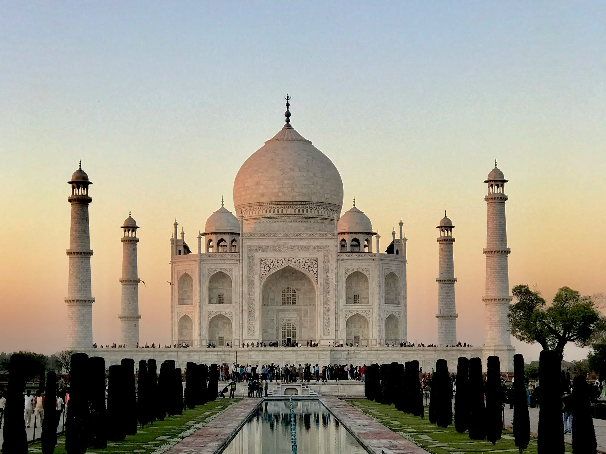 The Taj Mahal at sunset, mirrored in its long reflecting pool between rows of cypress trees, Agra