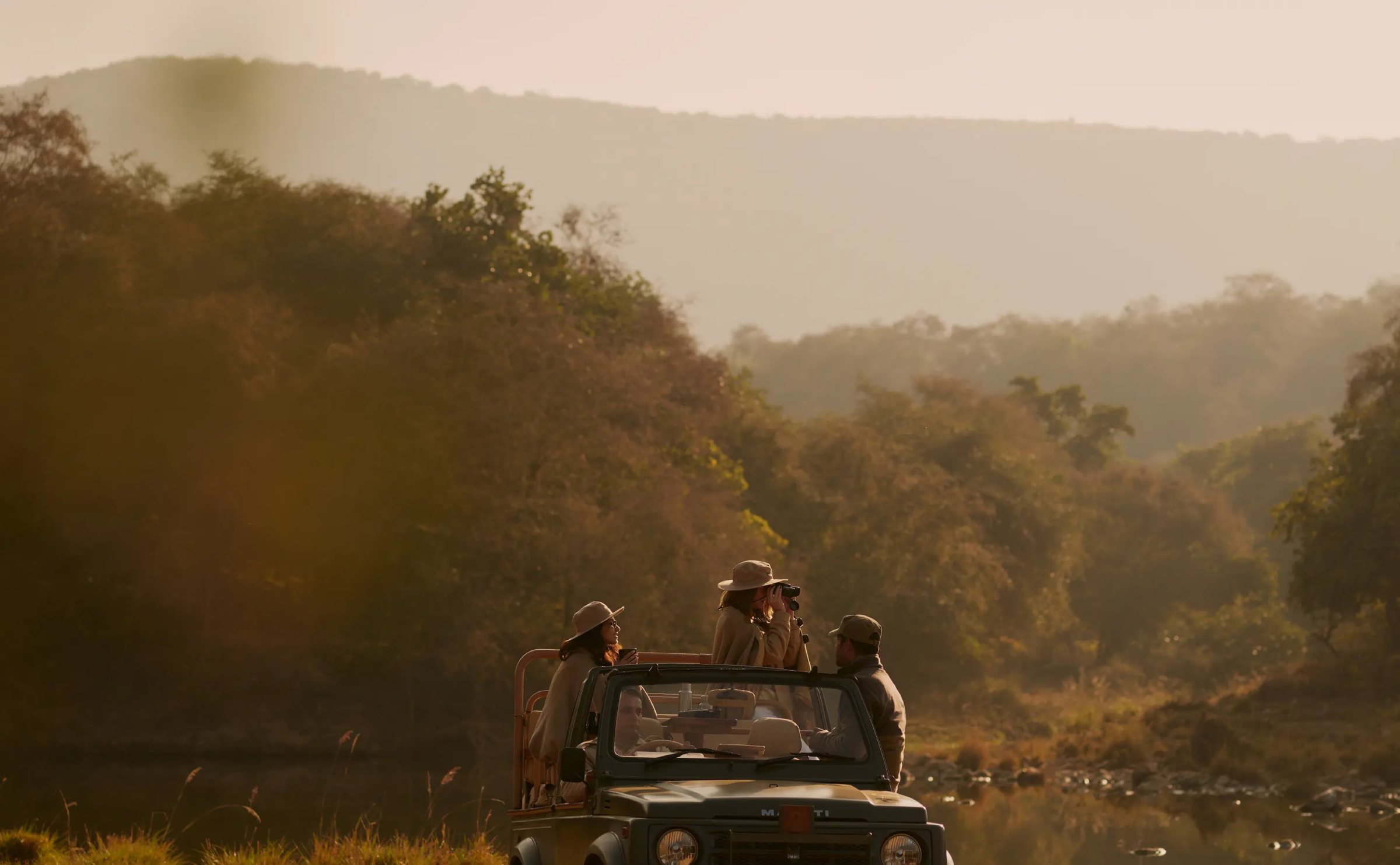 An open safari vehicle in wooded hills in the early light