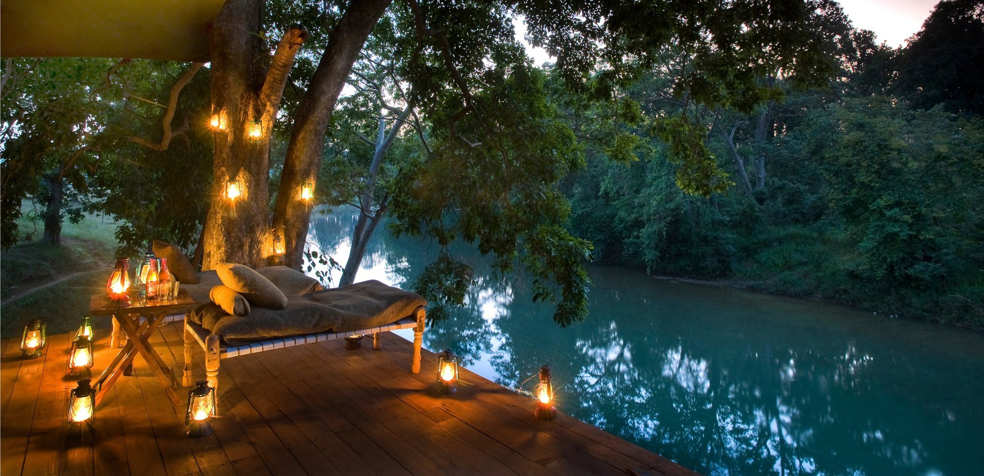 Lanterns lit on a riverside deck under a tree at Banjaar Tola