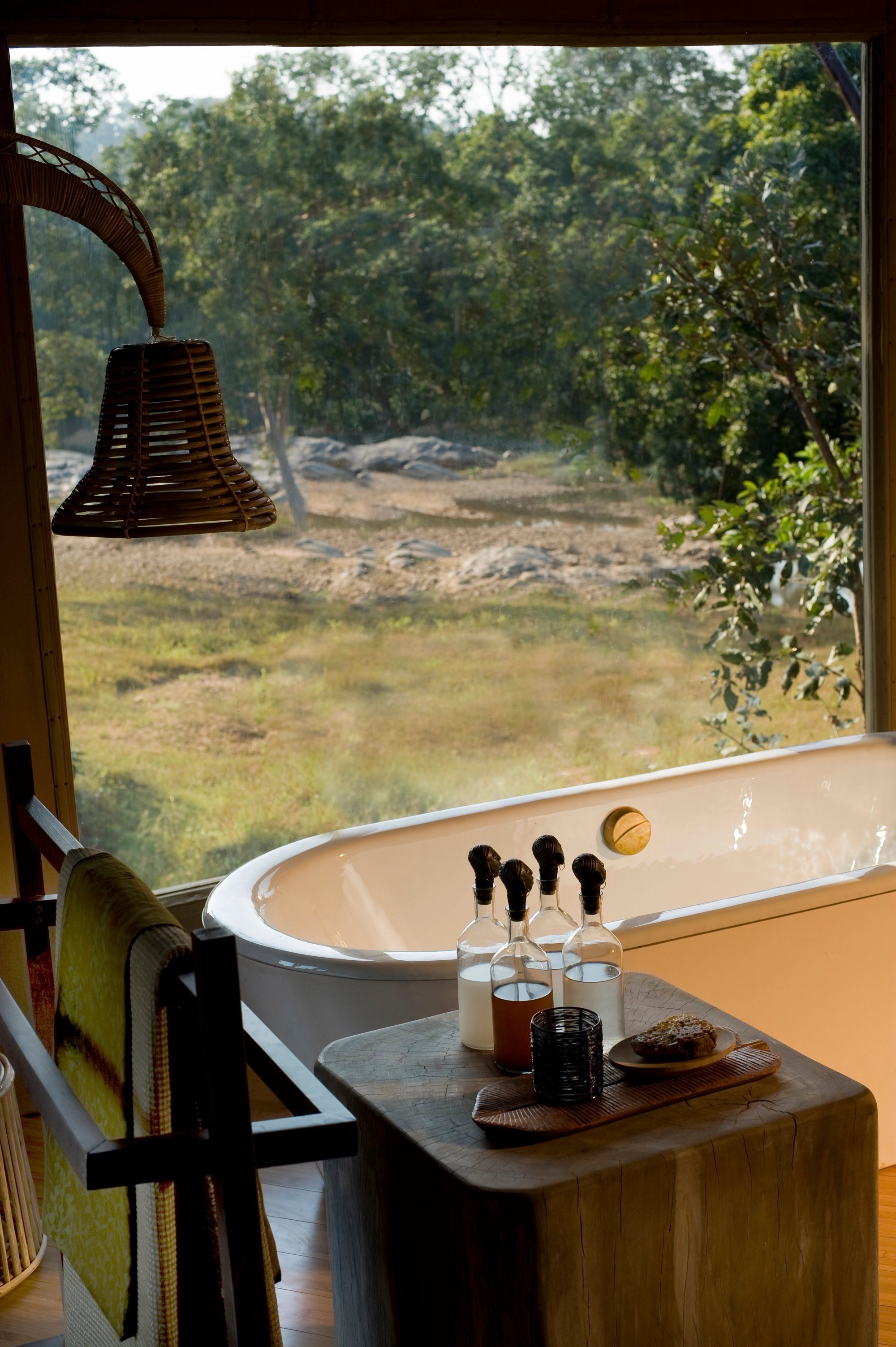 A freestanding bathtub by a window looking onto forest and meadow at Banjaar Tola
