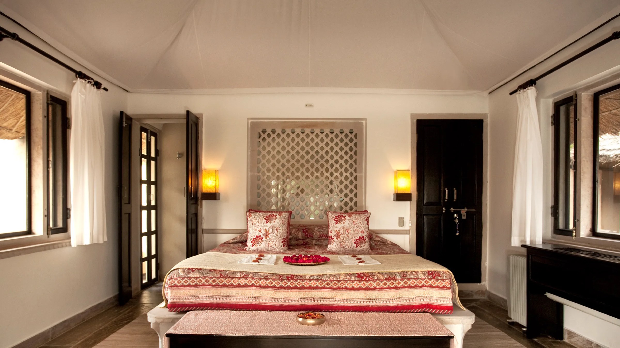 A cottage bedroom at Khem Vilas, with a carved stone screen behind a block-printed bed