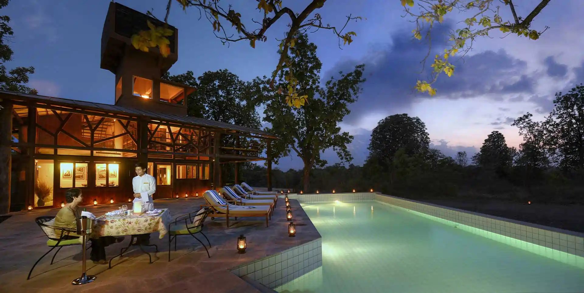 The pool and lodge buildings lit up at dusk at Pench Tree Lodge