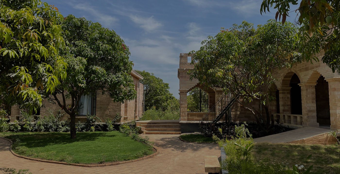 Lawns and mango trees in front of the stone buildings of Postcard Gir