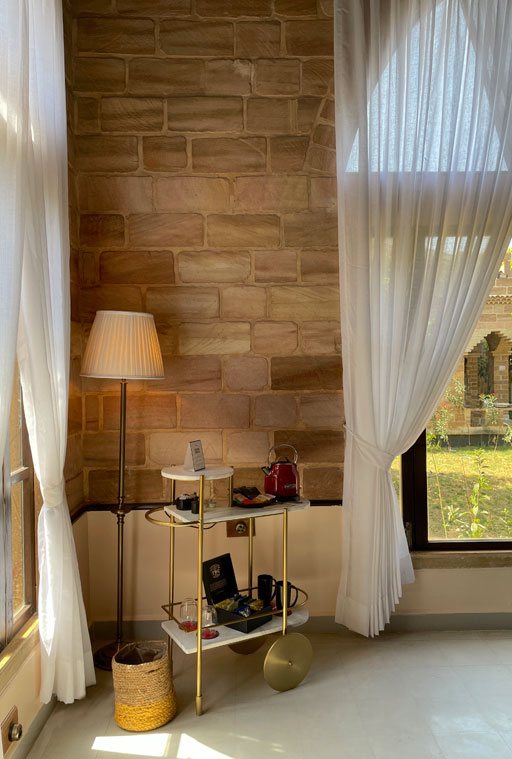 A corner of a room at Postcard Gir with stone walls, sheer curtains and a lamp