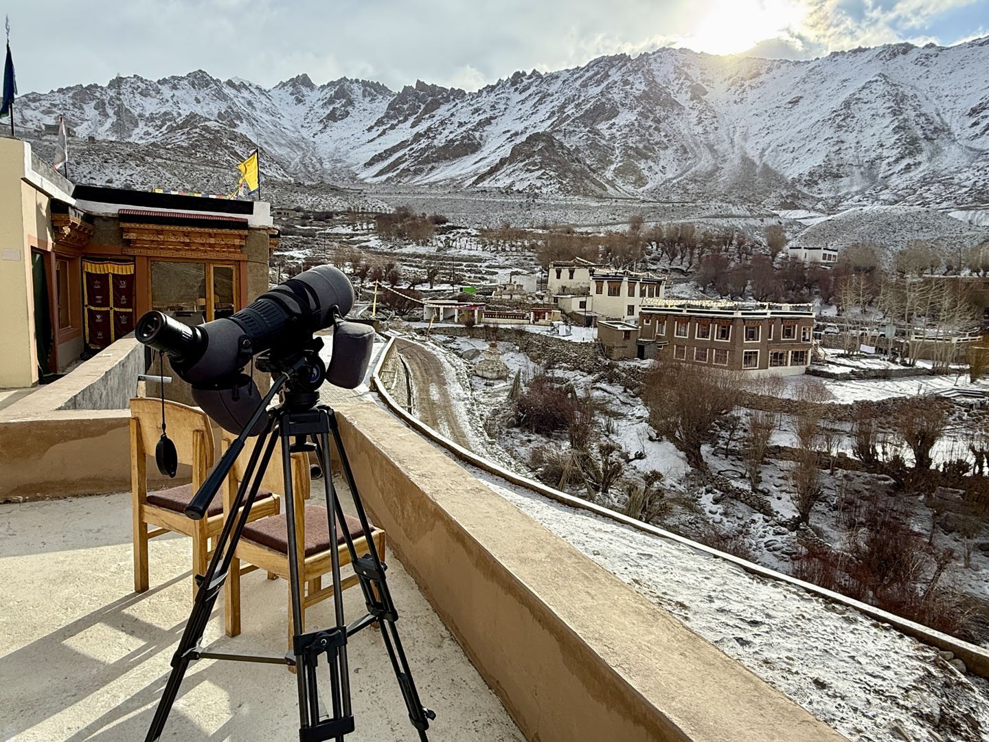 A spotting scope on a terrace above a snowy village and mountains