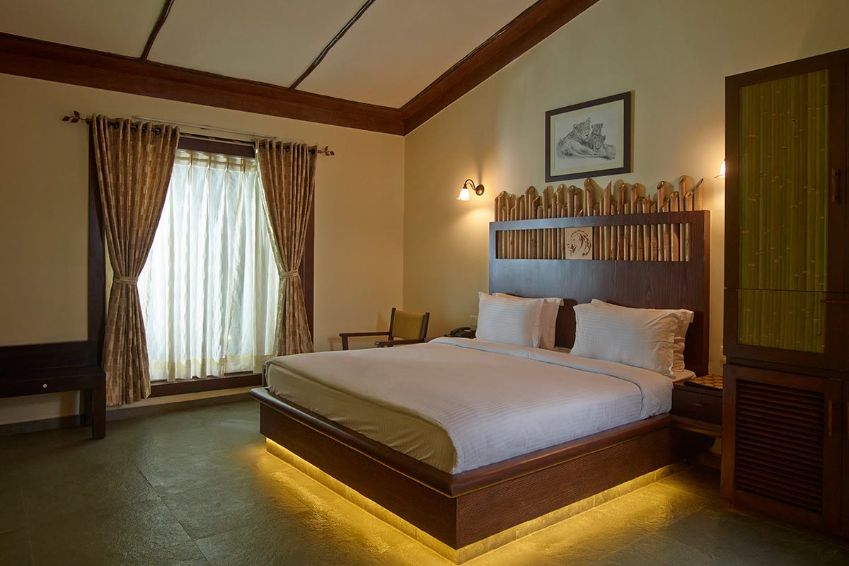 Guest room at Asiatic Lion Lodge, with a timber headboard and tall curtained windows