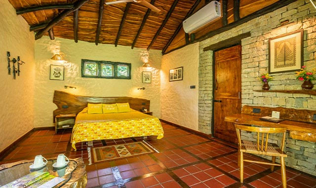 Room at Kanha Earth Lodge, with a timber roof, a stone wall and a terracotta floor