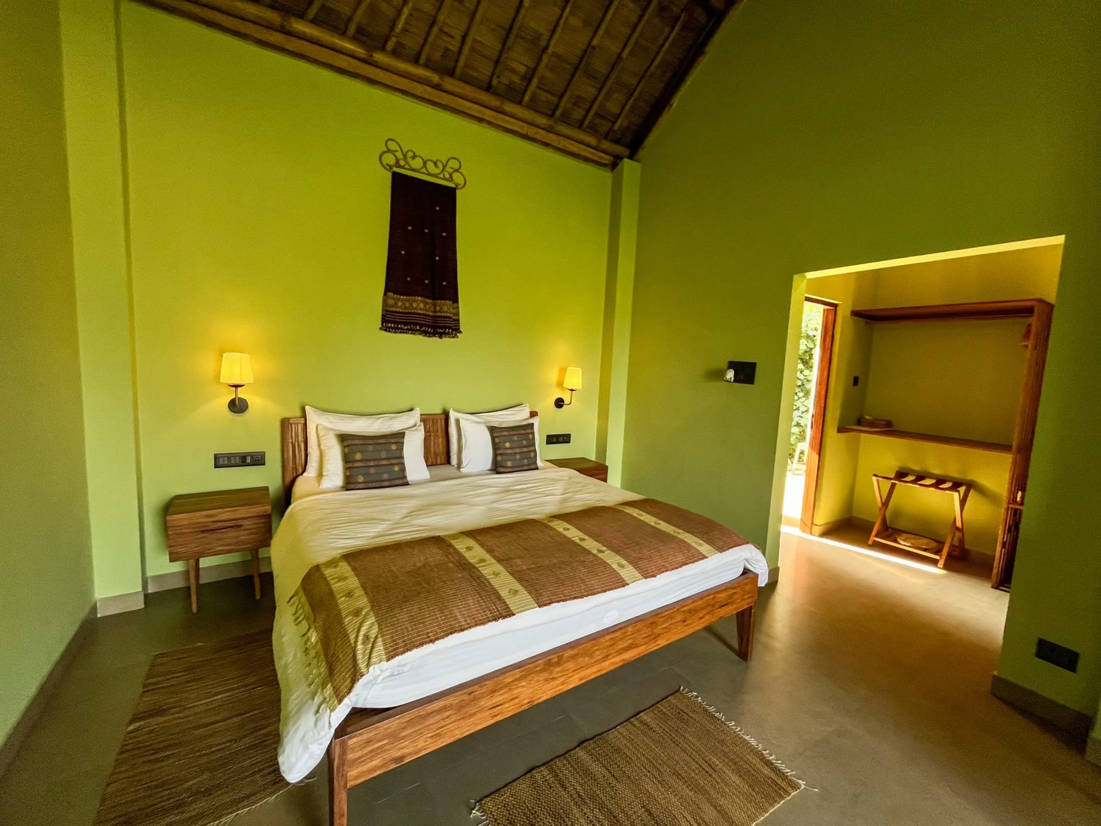 Room at Kathoni, Kaziranga, with green walls, a bamboo ceiling and a woven bedspread
