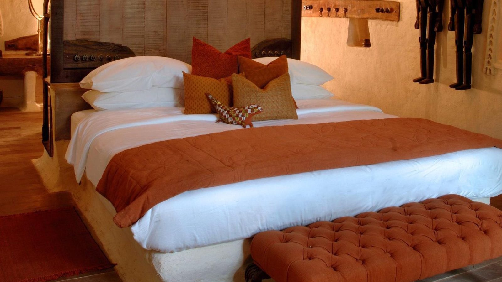 Cottage bedroom with an orange bedspread and ottoman at Mahua Kothi, Bandhavgarh