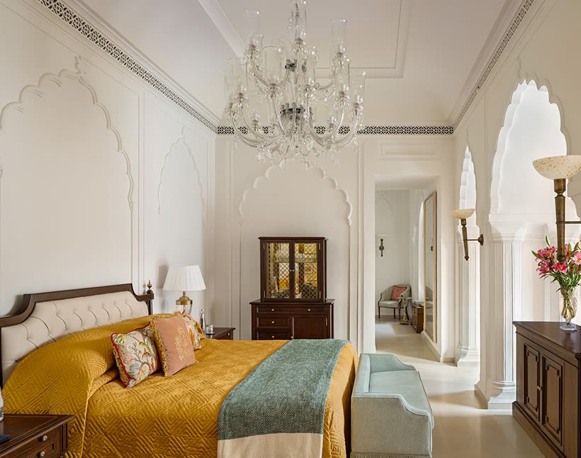 Bedroom of a suite at The Oberoi Rajgarh Palace, with a gold quilt and carved white arches