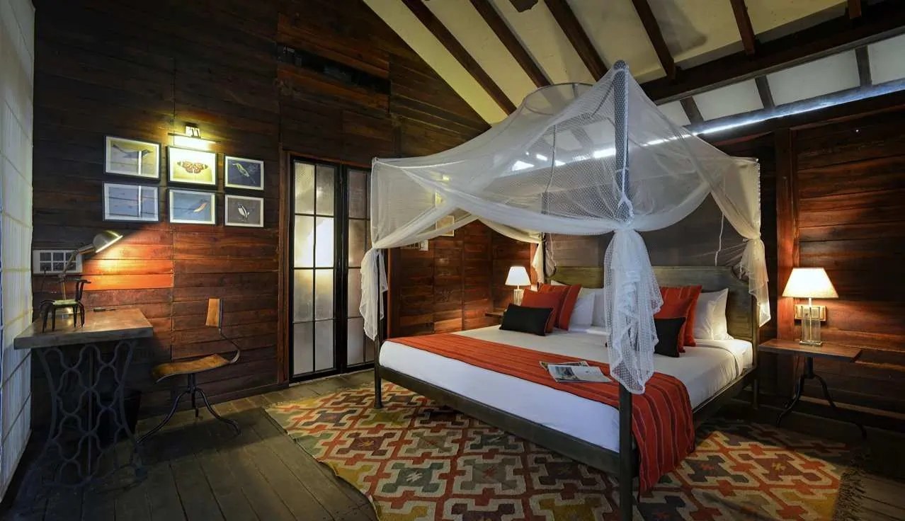 A tree-house bedroom at Pench Tree Lodge, with a netted four-poster bed, timber walls and a kilim rug