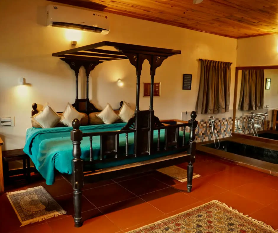 Room at RedEarth Kabini, with a carved four-poster bed and a sunken bath
