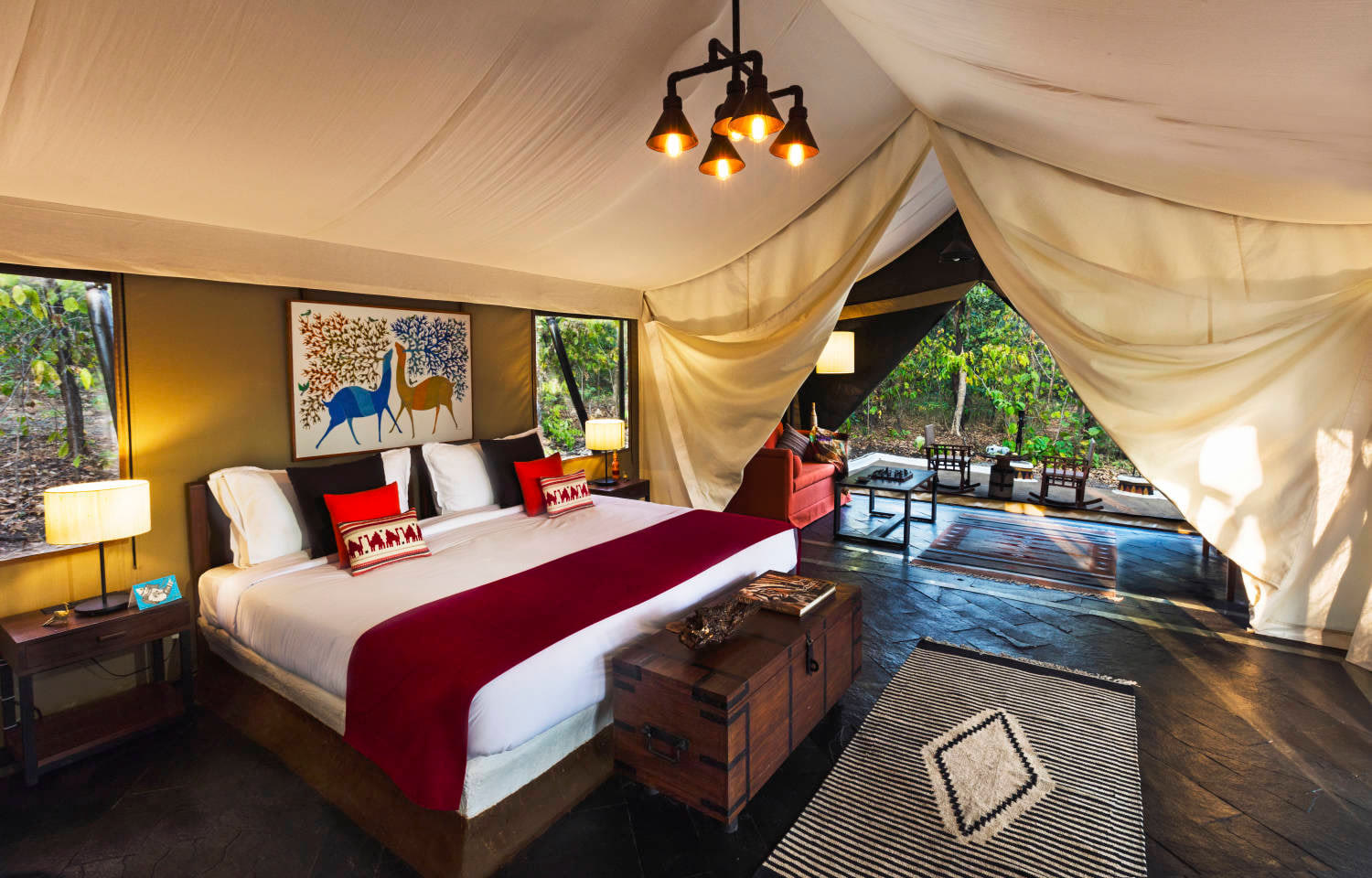 Luxury tent at Reni Pani Jungle Lodge, with a king bed, a Gond painting and the forest beyond