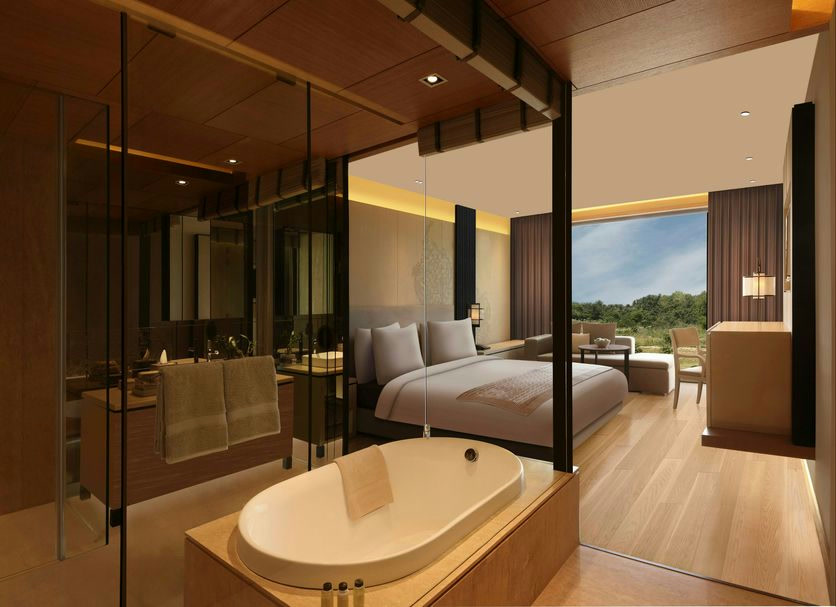 Bedroom at Roseate House, New Delhi, with a deep soaking tub behind glass and a wide window onto greenery
